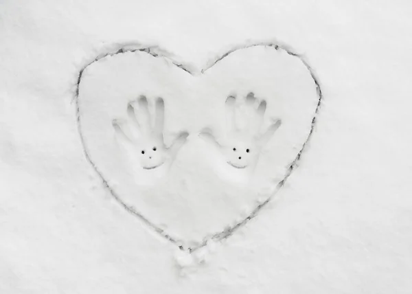 Top view of big heart drawn in the snow and two handprints with smile  in the middle. Fun and romantic concept. Copy space.