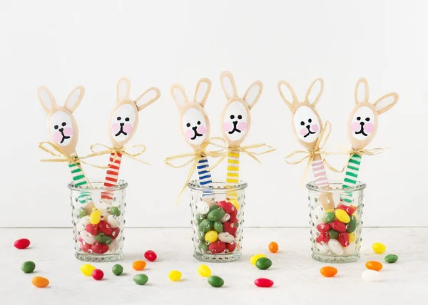 Handmade cute colorful bunnies made from wooden spoons in glasses with sweet candy eggs. Small gift or decor for Easter. Easy fun kids crafts concept.  Selective focus. Copy space.