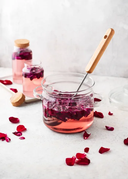 stock image Delicious sweet rose syrup in a glass cooking pot with pink petals in it. Homemade summer food concept. Selective focus. Copy space.