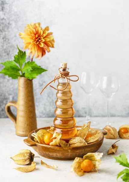 Delicious golden berries liqueur in a glass bottle. Homemade food and drink concept. (Physalis pubescens) Copy space.