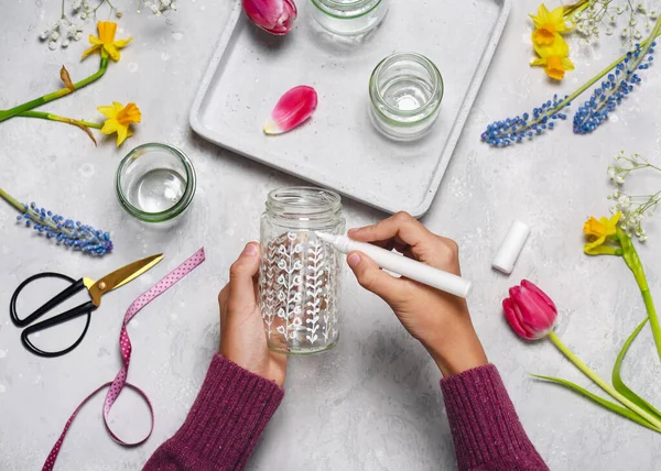 Step 3. Paint different flower motifs on a glass jar with white acrylic painter. Making spring decor for Easter or Mother\'s Day with kids. Top view