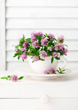 Güzel bir buket kırmızı yonca çiçeği ve kaliteli bir çay fincanı. Kırsal yaşam kır çiçekleriyle dolu. (Trifolium pratense) Seçici yumuşak odak.