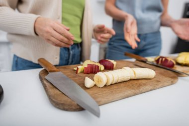 Cropped view of ripe fruits on cutting boards near blurred women in kitchen  clipart