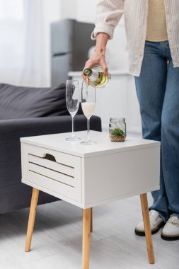 Cropped view of woman pouring champagne at home  clipart