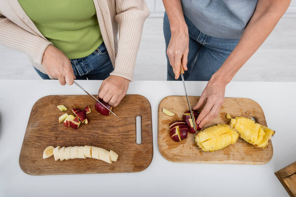 Top view of friends cutting fresh fruits on cutting boards in kitchen 