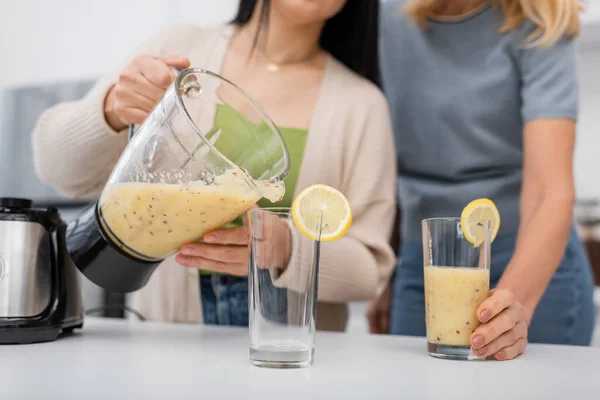 stock image Cropped view of blurred women pouring fruit smoothie in glasses with lemons at home 