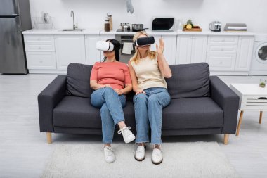 VR kulaklıklı kadınlar evlerinde oyun oynarken kanepede oturuyorlar. 
