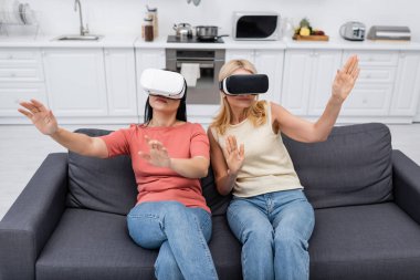 Sanal gerçeklik kulaklıklı arkadaşlar evdeki kanepede video oyunu oynuyorlar. 