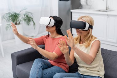VR kulaklıklı olgun bir kadın evdeki kanepede arkadaşının yanında video oyunu oynuyor. 