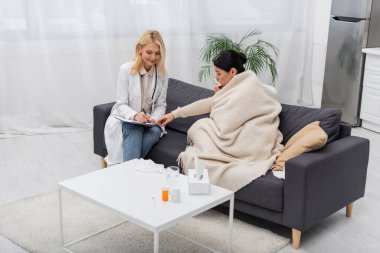 Hasta Asyalı kadın evdeki gülümseyen doktorun yanındaki panoya işaret ediyor. 