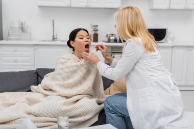 Dil bastırıcı kullanan doktor evde hasta bir Asyalı kadının boğazını kontrol ediyor. 