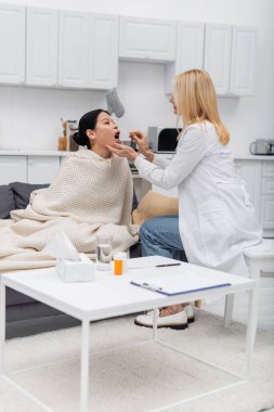 Evde Asyalı bir hastanın ağzının yanında dil basacağı tutan olgun bir doktor. 