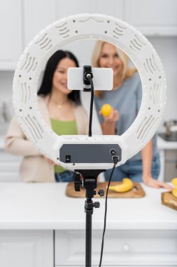 Yüzük lambası ve akıllı telefon. Mutfakta bulanık blog yazarları ve meyveler var. 