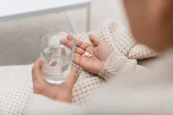 Cropped view of woman holding glass of water and pills at home 