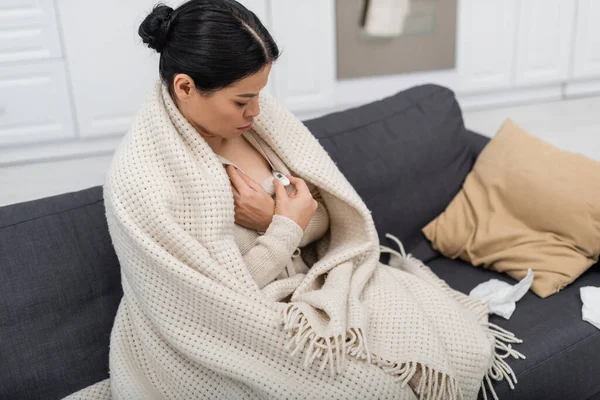 病気アジアの女性で毛布見ますで温度計オンソファホーム — ストック写真