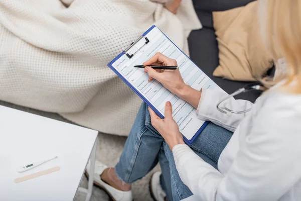 stock image Cropped view of doctor writing on clipboard near electronic thermometer at home 