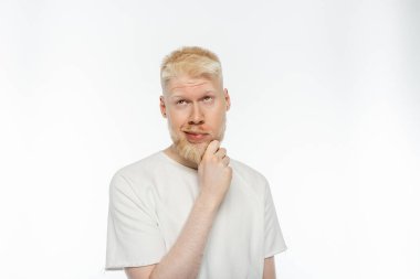 pensive albino man in t-shirt touching beard while thinking on white background clipart