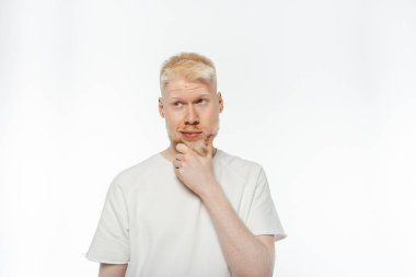 Tişörtlü albino adam beyaz arka planı düşünürken sakala dokunuyor.