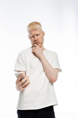 Düşünceli albino tişörtlü adam akıllı telefon kullanıyor ve sakala dokunuyor. 