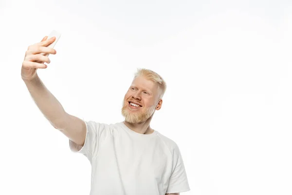 stock image cheerful albino man in t-shirt taking selfie on smartphone on white background