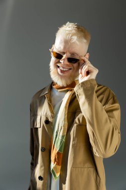 Güneş ışığı, mutlu albino adamın yüzüne vuruyor şık güneş gözlüklerini ayarlıyor ve gri renkte göz kırpıyor. 