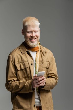 Şık gömlekli ve ipek eşarplı neşeli albino adam. Gri renkli telefondan izole edilmiş akıllı telefon. 