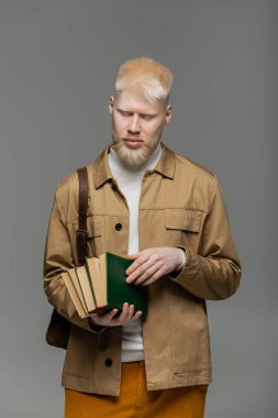 Sırt çantalı sakallı albino öğrenci gri üzerine kitap tutuyor.