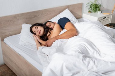 Young man hugging sleeping girlfriend on bed at home 
