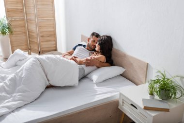 Bearded man hugging girlfriend in pajama while relaxing on bed 