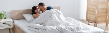 Man kissing brunette girlfriend on bed at home, banner 