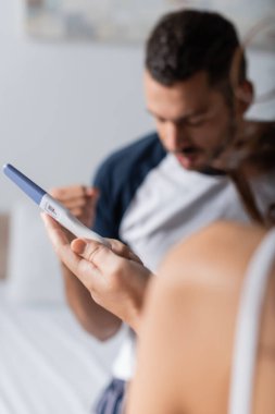 Blurred woman holding pregnancy test near blurred man at home 
