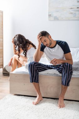 Upset man holding pregnancy test near blurred girlfriend in bedroom 