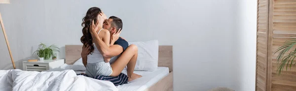 Young man in pajama kissing sexy girlfriend on bed at home, banner
