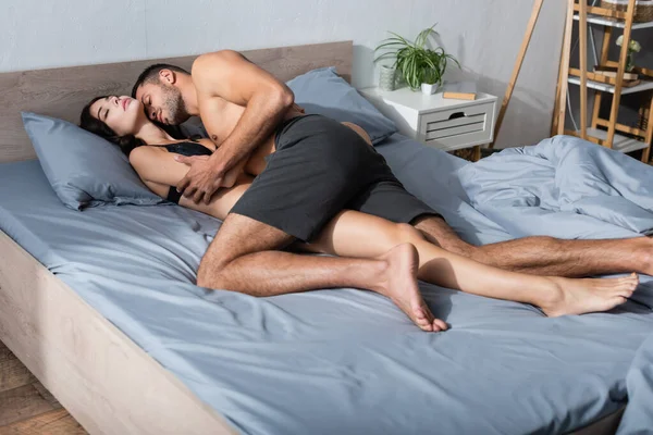 Muscular man kissing sensual girlfriend in underwear on bed