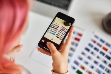 cropped view of young pink haired woman taking photos of paper with small images on it for her work clipart