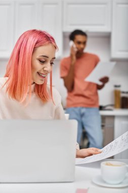 focus on jolly woman working next to her blurred african american boyfriend talking by phone clipart