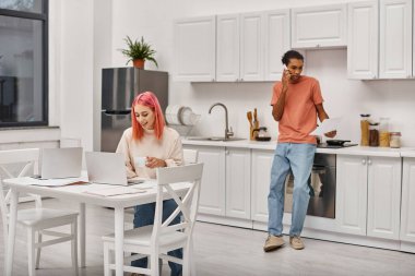 Bilgisayarda çalışan neşeli bir kadın. Odaklanmış Afrikalı Amerikalı erkek arkadaşının yanında. Telefonla konuşuyor.