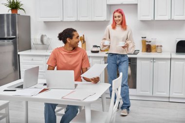 Elinde kahve fincanları olan güzel kız arkadaşına gülümseyen neşeli Afro-Amerikalı bir adam.