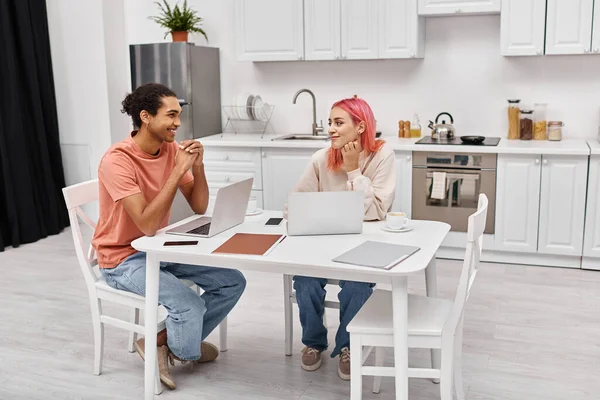 stock image cheerful beautiful interracial couple in homewear working on their laptops and smiling at each other