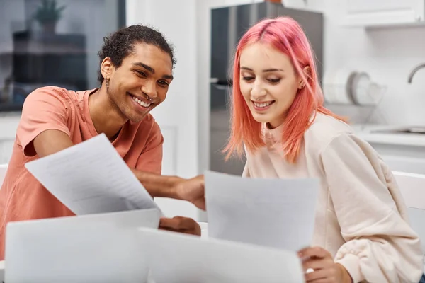 stock image attractive joyous multiracial couple in cozy homewear looking at paperwork while working remotely