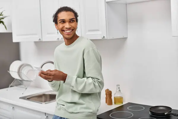 stock image handsome joyful african american man in white casual sweater holding smartphone and looking away