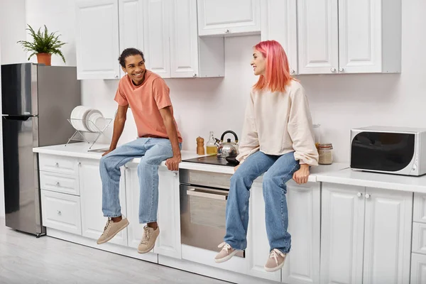 Joyous Appealing Multiracial Couple Homewear Sitting Kitchen Counter Smiling Each Royalty Free Stock Images
