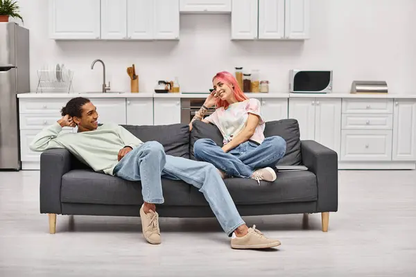 リビングルームでソファーでリラックスし お互いに微笑み合う楽しい異人種間のカップル ロイヤリティフリーのストック画像
