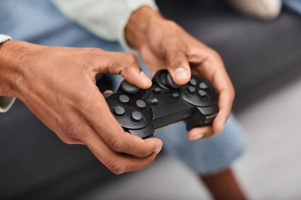 リビングルームでゲームをしている若いアフリカ系アメリカ人男性の手で現代のゲームパッドの見た目 ストック画像