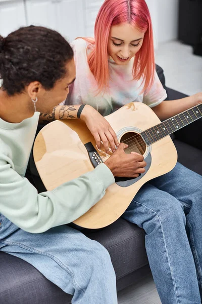 良い見栄えのジョリーアフリカ系アメリカ人男性は 彼のピンクの髪のガールフレンドを教えています ギターを弾く方法 ストック画像