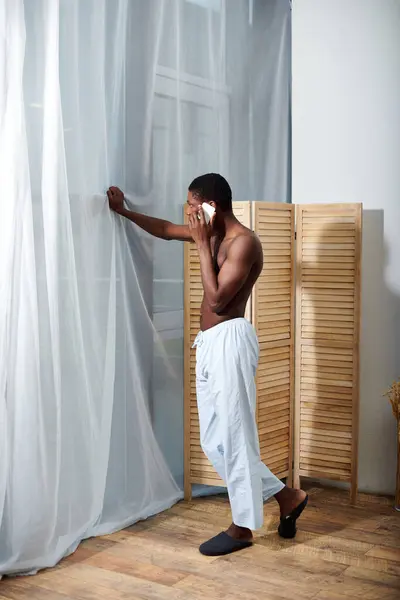 stock image A young African American man standing in front of a curtain, talking on a cell phone.