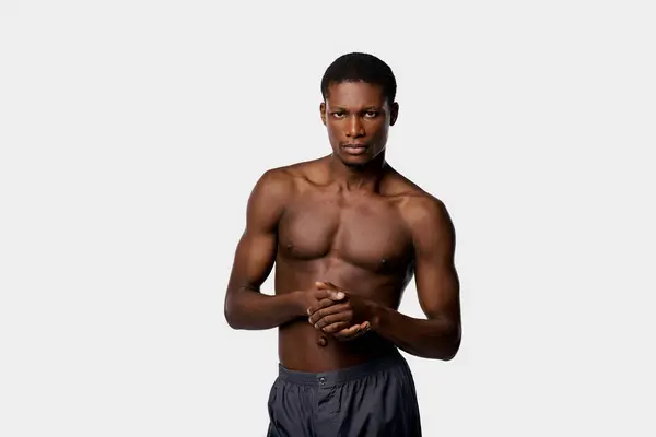 stock image African American man stands confidently with no shirt against a stark white backdrop in a studio setting.