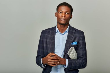 Takım elbiseli ve mavi gömlekli Afro-Amerikan bir adam gri bir arka plana karşı güven ve profesyonellik yayıyor..