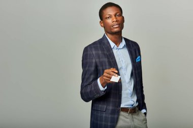 Kareli ceketli afro-amerikan bir işadamı gri arka planda bir iş kartı tutuyor..