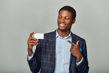 Resmi giyinmiş genç bir Afrikalı Amerikalı işadamı gri bir arka plana gururla işaret ediyor..